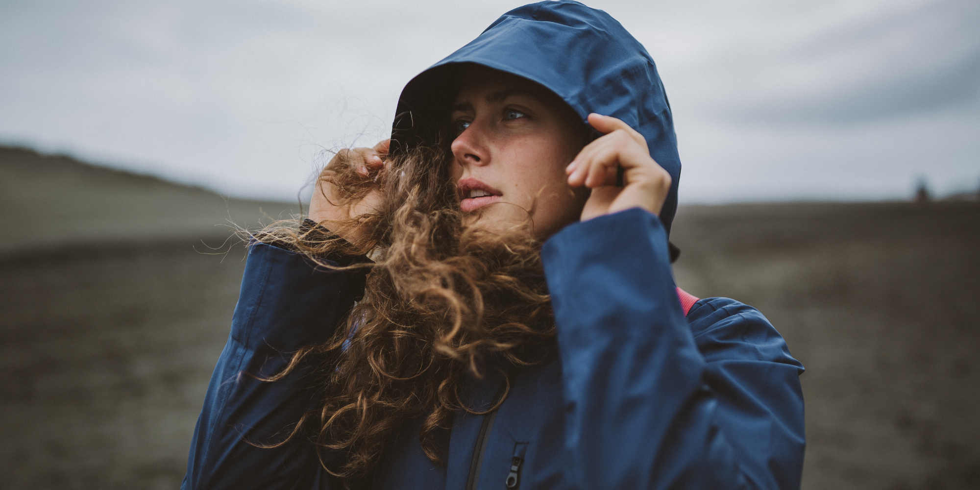 Person wearing a blue raincoat with hood in a landscape setting

