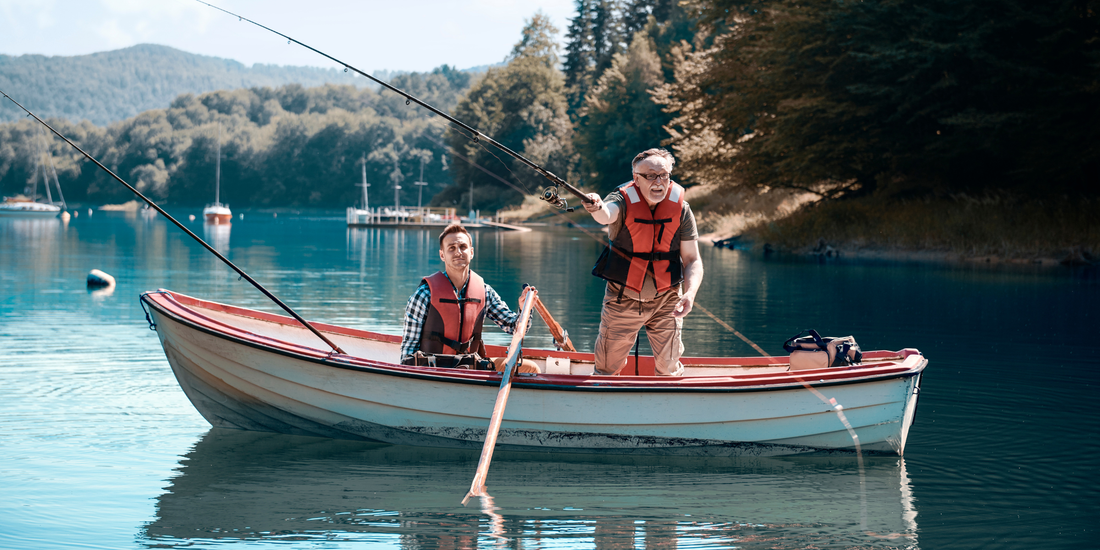 Two people in a boat on a calm lake with trees and mountains in the background

